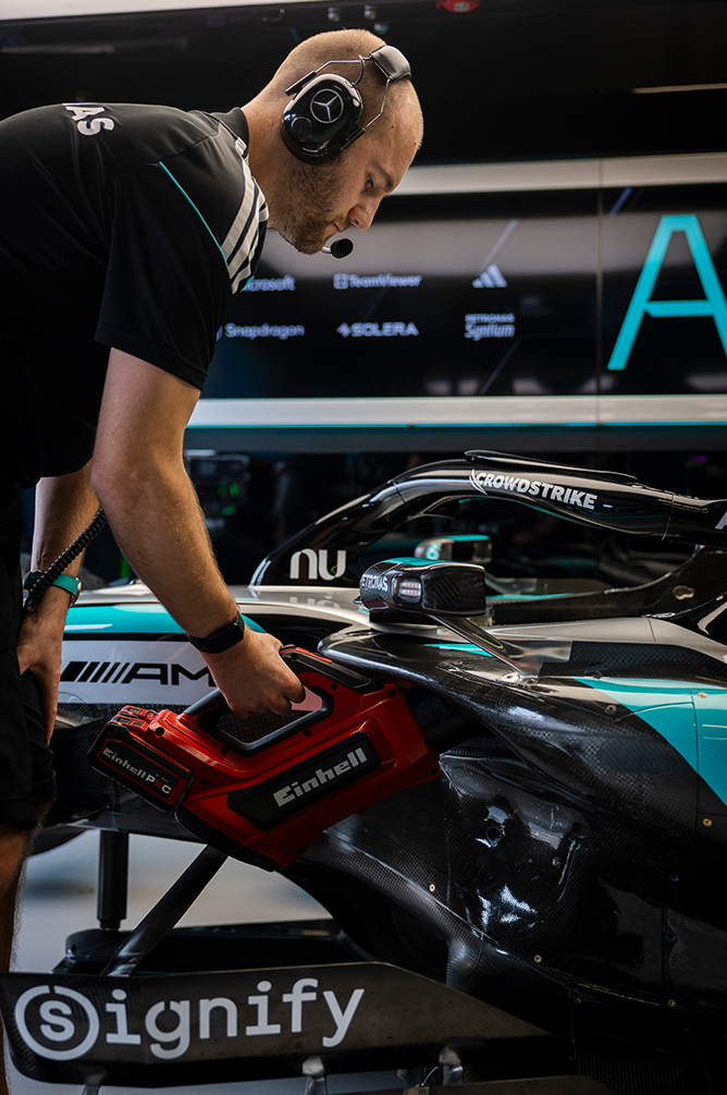 Formula 1 mechanic working with a tool on a race car in the pit.